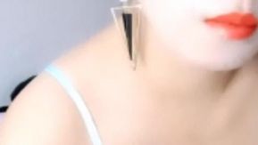 Uma jovem bonita de lábios vermelhos, vestindo uma roupa sexy transparente, está fazendo sexo com um vibrador, vibrando e dedilhando sua buceta, fodendo-a forte e rápido