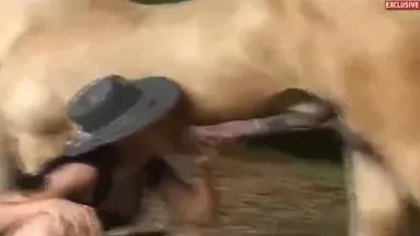 Handsome amateur cowgirl in high boots and black dress with a horse in the stable