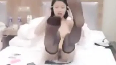 A fair-skinned and slender girl performs a two-person show with her limbs covered by a hooded man on the bed with a high-end vibrator vibrating her pussy.